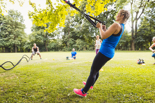 Side view of fitness young woman doing stretching exercise with resistance band in the park