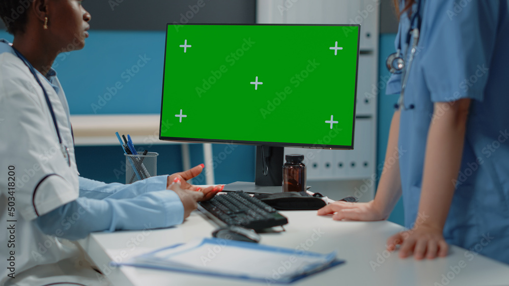 Poster close up of computer with horizontal green screen on desk while doctor and nurse talking. medical te