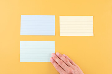 hand putting blank writing paper and two empty papers on a yellow background. space for text.