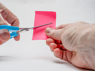 Man cutting pink craft paper with blue left handed scissors selected focus