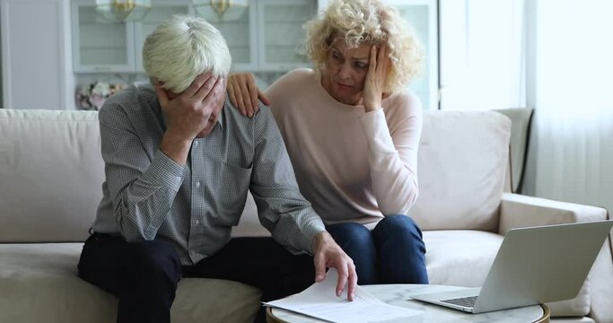 Mature couple sit on sofa read received paper notification feel stressed looking desperate, bank debtor spouses get legal reasons for eviction, non-payment of rent, bankruptcy, bad news from relatives