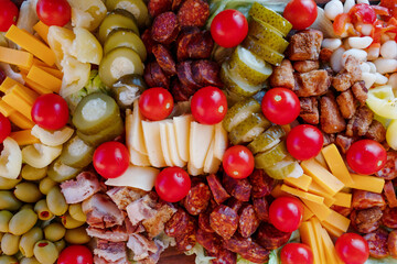 cherry tomatoes, sweet peppers,  pickled cucumbers, pickled garlic, olives,  sausage, different cheese, bacon on wooden plate. Snack food