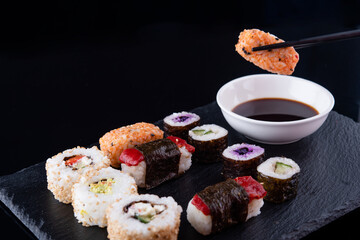 Close up of delicious japanese food with vegetarion sushi rolls  with beetroot and cucumber  with black chopsticks  and  soy sauce on black background