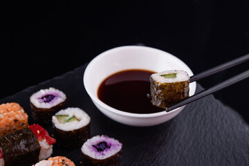 Close up of delicious japanese food with vegetarion sushi rolls  with beetroot and cucumber  with black chopsticks  and  soy sauce on black background