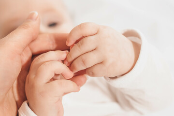 Baby holds and looks at mom hand. The emotional bond between mother and child. Development of motor...