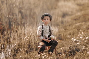 Naklejka na ściany i meble Boy in vintage clothes with a chick in the field. A boy in suspenders