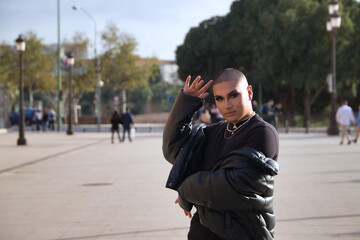 Non-binary person, young and South American, heavily make up, dressed all in black, posing on vacation in a European city. Concept queen, lgbtq+, pride, queer.