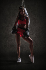 Fototapeta na wymiar Athletic woman in red shorts and top posing near the bag. Boxing and mixed martial arts concept