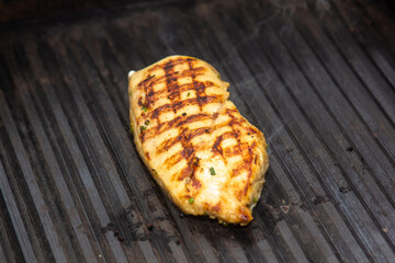 Lean healthy chicken breasts grilling over the hot coals on a portable BBQ with fresh tomatoes and potatoes for a healthy low fat meal
