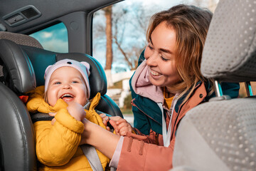Portrait of happy caucasian mother prepares her little smiling cute child for a trip by car. A...