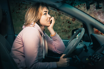 A scared nervous woman is sitting behind the wheel of a left-hand drive car and bites her nails....