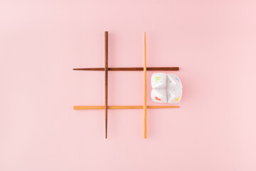 Tic tac toe game with wooden food chopsticks and paper origami fortune teller on pink background. Minimal concept.