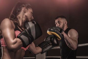 Athletic woman in red shorts and top is boxing with a trainer. Boxing and mixed martial arts...