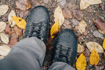 Close up detail photo of hiking or trekking boots in muddy autumn trail. Mountain leather shoes on dirty terrain, wet ground and stepping into water. Waterproof shoes using goretex technology.