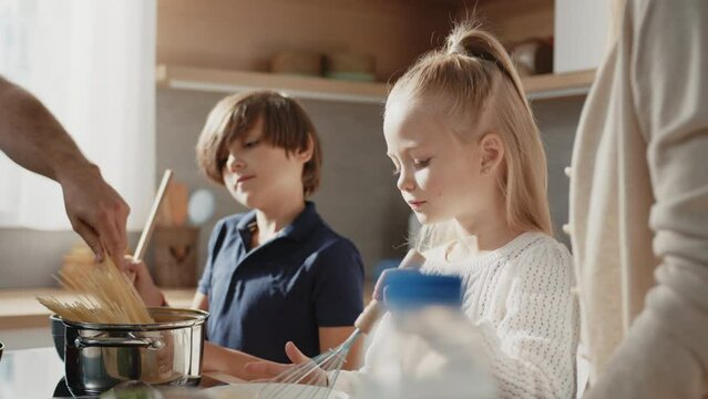 Close up of cute son and daughter learn how to cook omlet, having fun, helping parents in the kitchen. Caucasian family with little kids prepare breakfast together at home.