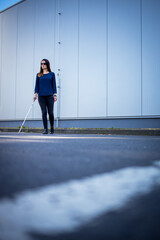 Blind woman walking on city streets, using her white cane to navigate the urban space better and to...