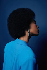Fototapeta na wymiar Minimal fashion shot of young black woman with puffy natural hair posing against blue background