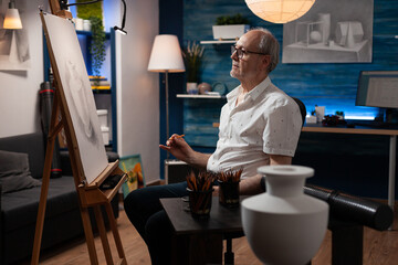 Retired artist holding pencil drawing artwork admiring progress in the evening sitting down in home...