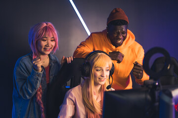 friends encouraging blonde Caucasian girl while playing online game medium shot esport indoors neon light. High quality photo © PoppyPix