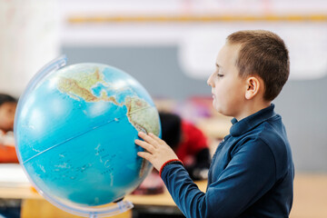 A schoolboy searching for places on the globe at geography class.