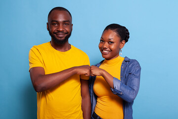 Portrait of smiling couple bumping fists together on camera, celebrating successful teamwork with...
