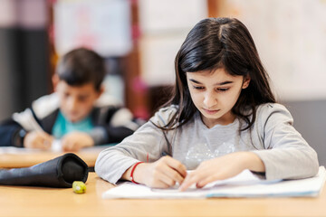 A schoolgirl writing down answers in notebook in school.