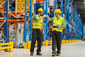Two warehouse workers having fits bump for teamwork. - obrazy, fototapety, plakaty