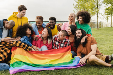 Happy diverse friends holding LGBT rainbow flag having fun together outdoors - Focus on right man with leg prosthesis - obrazy, fototapety, plakaty