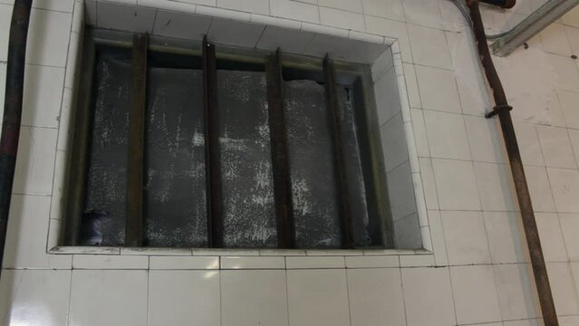 A scary prison cell with bars on the windows. The creepy room has tiled walls and rusty grates