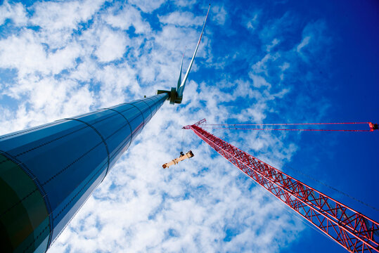 Construction of Wind Turbine Tower using Big red crane under beautiful blue sky. Clean alternative energy concept to reduce global warming and climate change for  sustainable growth and developement. 