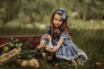 A girl in vintage clothes is holding a goose. Green grassy background.