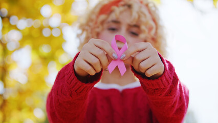 Young blond Caucasian woman shows pink ribbon to the camera breast cancer support concept copy...