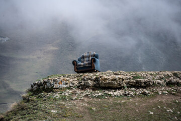 an easy chair on a rock against the backdrop of mountains and a gorge and floating white clouds