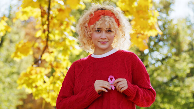Young blond curly haired woman holds pink ribbon breast cancer support concept copy space outside Pink October . High quality photo