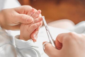 mother cuts baby's fingernails with special children's scissors. close up. manicure for newborns. grey background