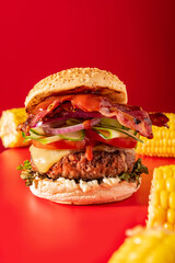 Bold fresh cheeseburger loaded with lettuce, cucumber, tomato and bacon on vibrant red