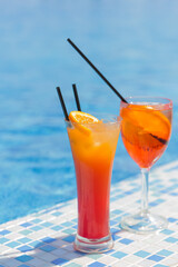 Two citrus orange cocktails with straws in the summer by the pool