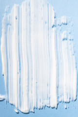 Sample smear of a white cosmetic product on a blue background flat lay. Body cream, skin lotion close-up.