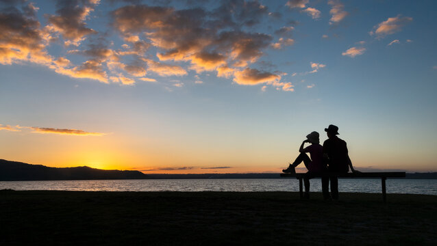Silhouette image of a couple sitting on a bench and watching sunset, Rotorua, New Zealand.
