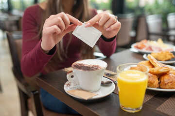 Breakfast with cappuccino, sweets and orange juice, Woman opening one sugar