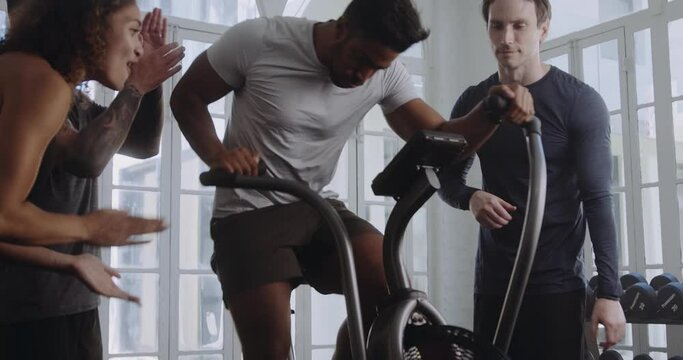 Biracial male reaching his personal best and working hard on the bike in a modern style gym. Friends motivating, cheering him on.
