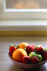 Pink bowl filled with fresh apples, oranges and strawberries on wooden table. Selective focus.