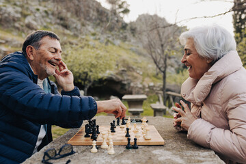 Cheerful senior couple playing chess in a park