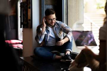 Obraz premium Young man sitting and listening the music. Portrait of happy bearded man listening music with earphones while singing song.