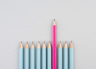 Blue pencils in a row, one pink pen is standing out, be different, leadership and teamwork concept