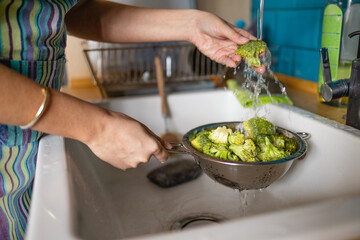 Woman washes broccoli in the sink