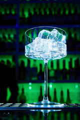 Empty glass with ice on bar counter on green background. Close-up, selective focus