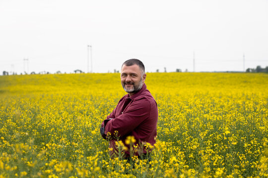 Portrait Of Smiling Middle Age Farmer Standing In Rapeseed Field Examining Crop.