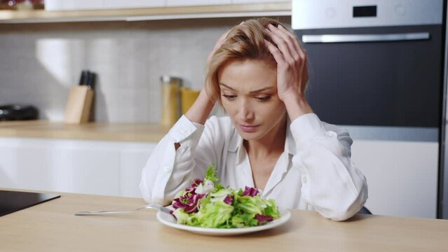 Close up woman sitting at table looking sad and bored with diet don't want to eat salad. At the kitchen. Food. Portrait. Slow motion