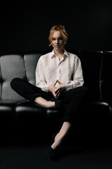 Stylish young businesswoman sitting on sofa and looking at camera